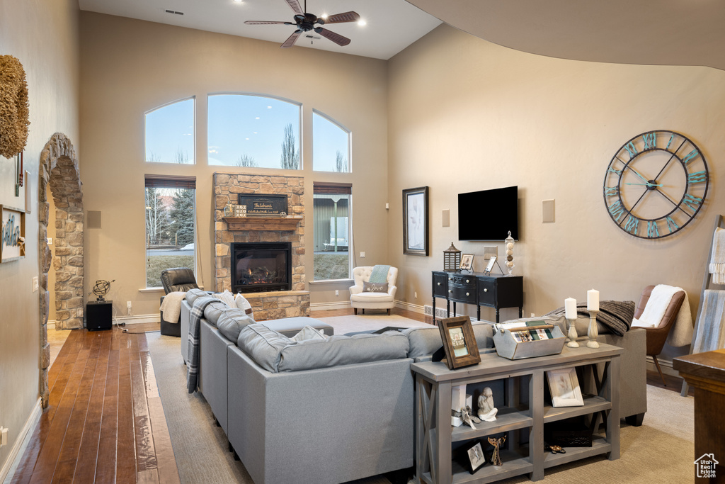 Living area featuring baseboards, light wood-type flooring, a stone fireplace, a high ceiling, and a ceiling fan