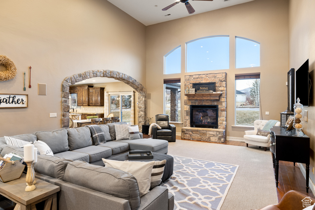 Living room featuring arched walkways, a stone fireplace, wood finished floors, and a healthy amount of sunlight