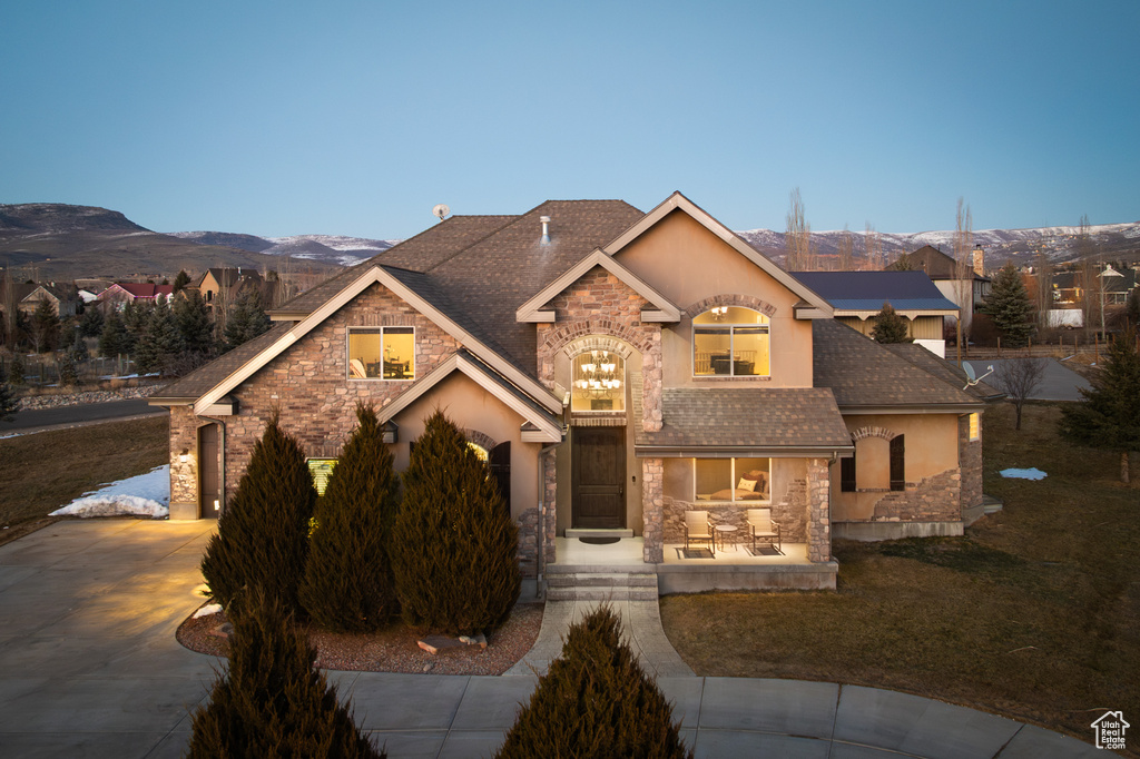 View of front of home featuring driveway, a shingled roof, stucco siding, stone siding, and a mountain view