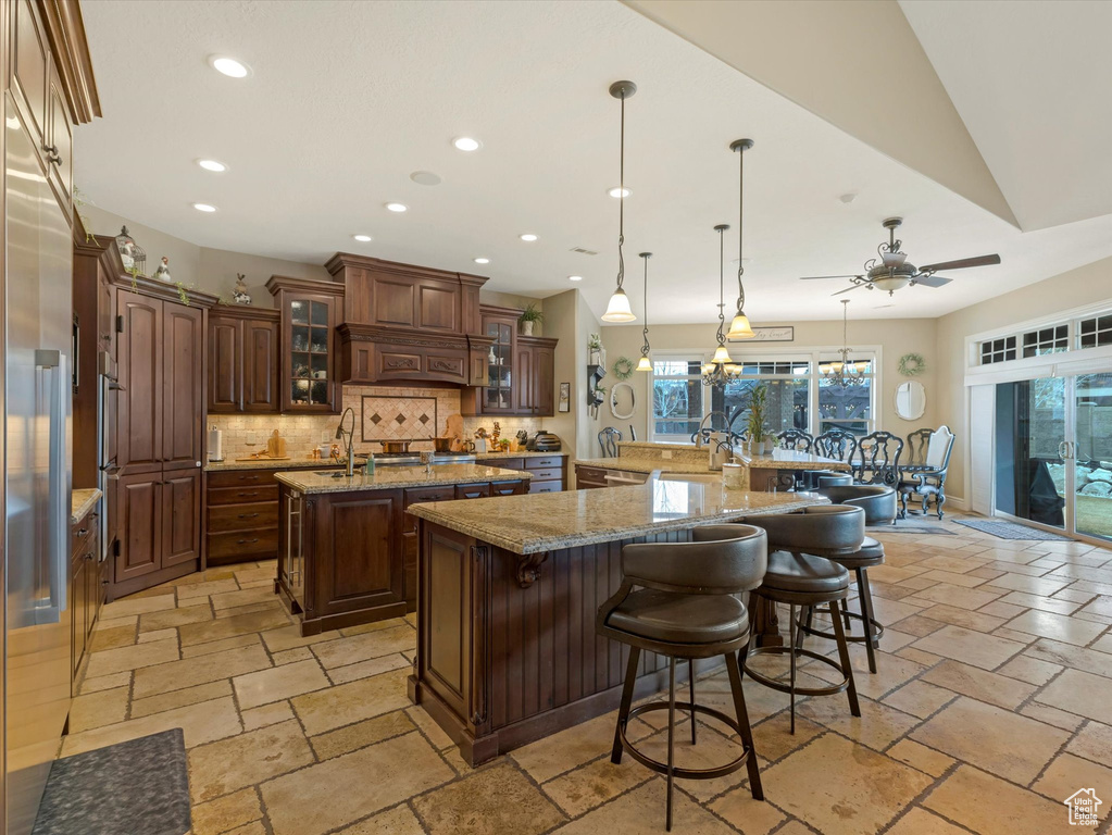 Kitchen featuring stone tile flooring, decorative backsplash, a large island with sink, and recessed lighting