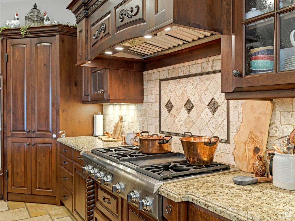 Kitchen featuring glass insert cabinets, stone tile flooring, stainless steel gas stovetop, decorative backsplash, and custom exhaust hood