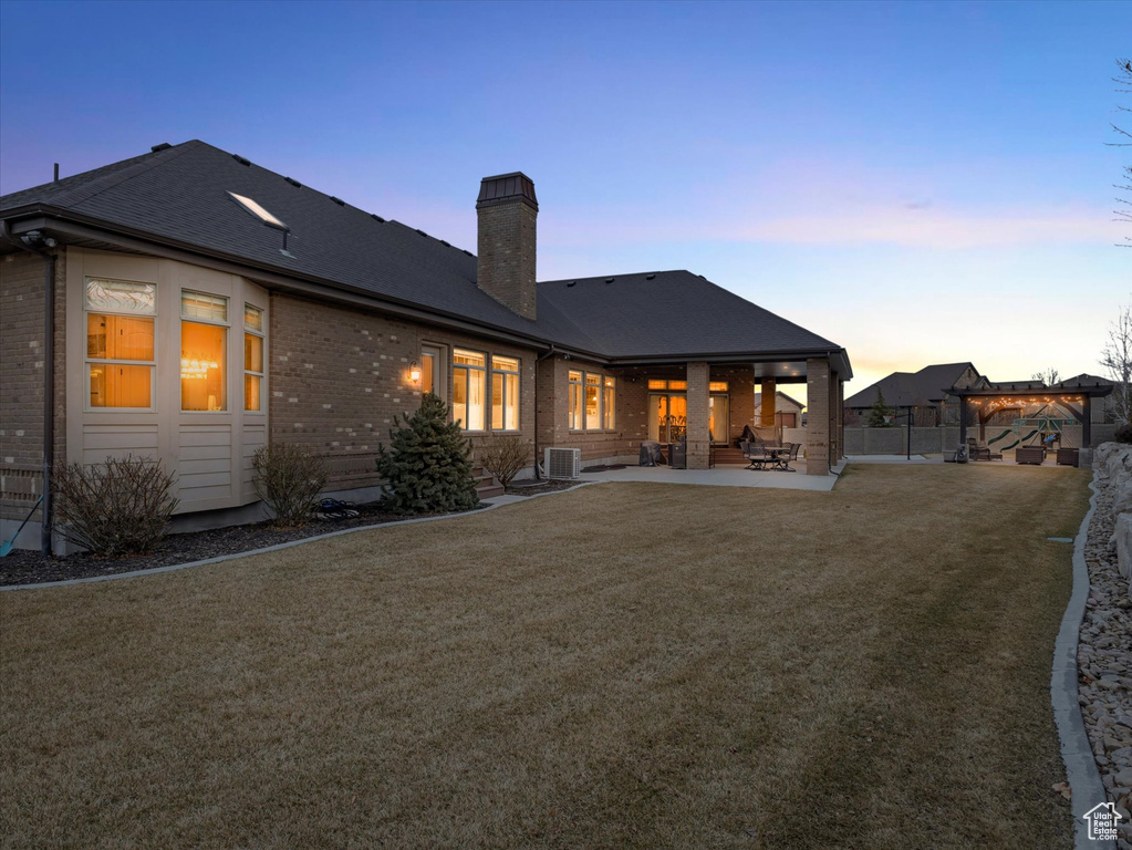 Rear view of house featuring brick siding, central AC, a chimney, a yard, and a patio