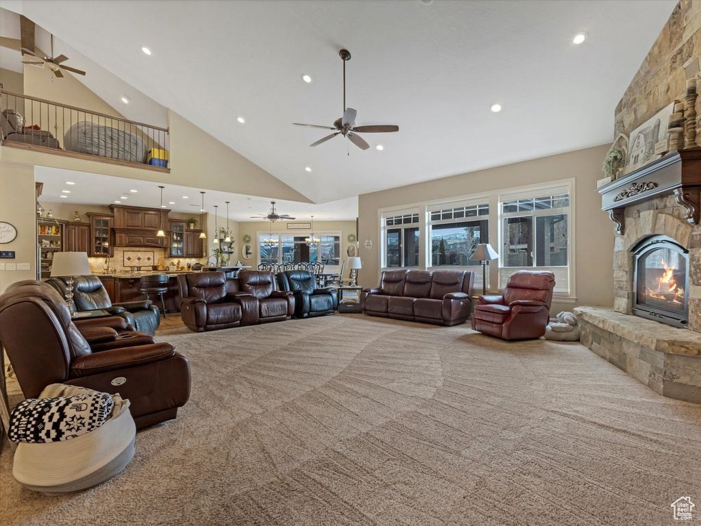 Living area featuring a stone fireplace, a ceiling fan, carpet, and high vaulted ceiling