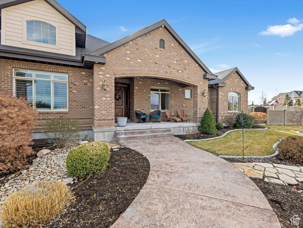 View of front of home featuring a front lawn, fence, covered porch, a shingled roof, and brick siding