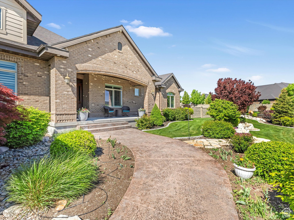 Entrance to property with brick siding, covered porch, a lawn, and a shingled roof