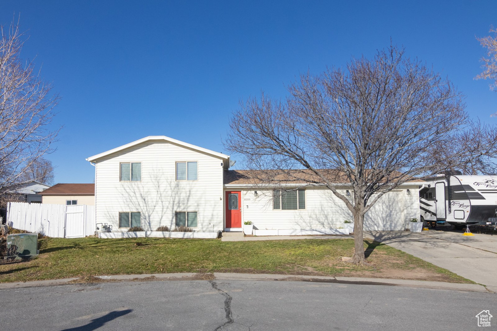 Tri-level home featuring concrete driveway, a front yard, and fence