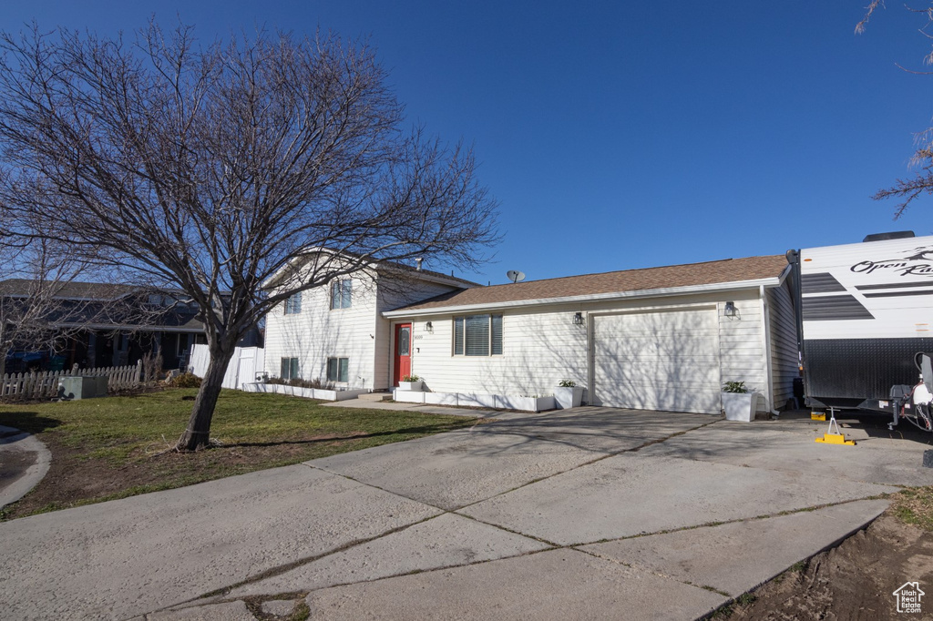 View of front facade featuring a garage, concrete driveway, a front yard, and fence