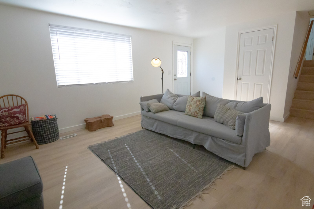 Living room featuring stairs, light wood-style floors, visible vents, and baseboards