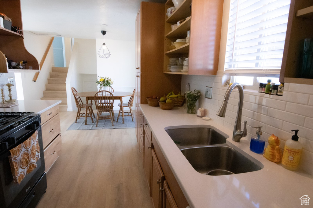 Kitchen with black gas range oven, light wood-style flooring, light countertops, and open shelves