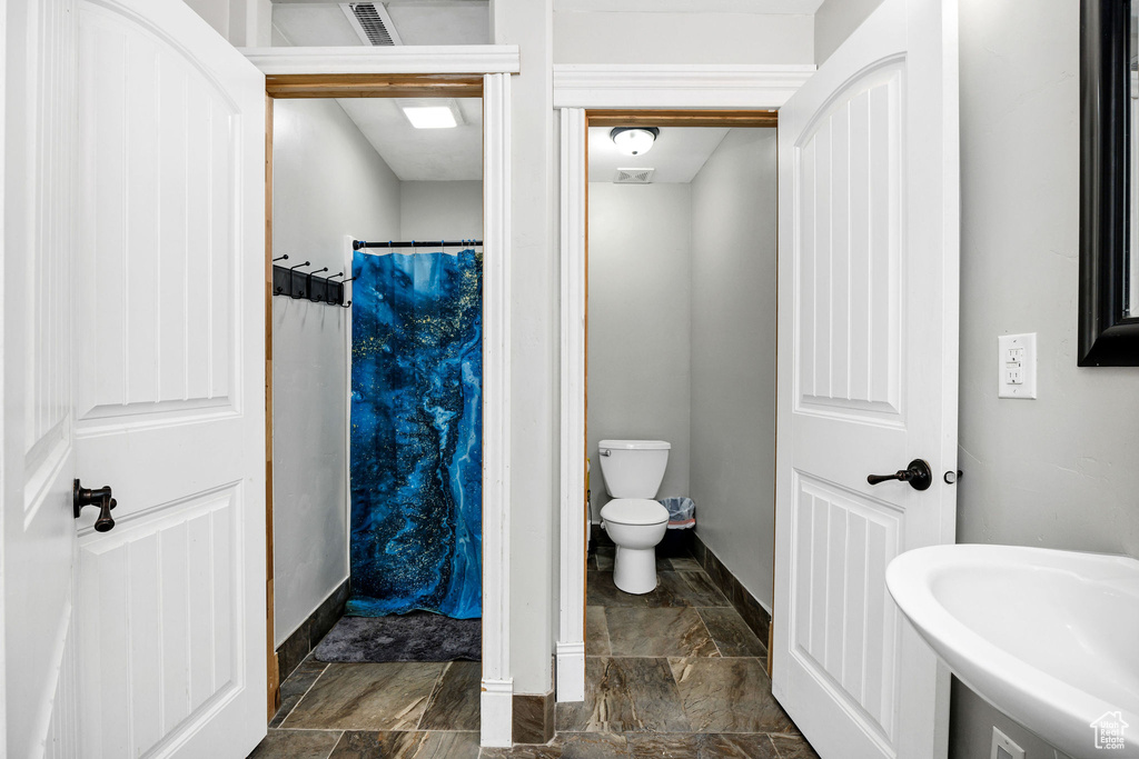 Full bathroom featuring a shower with curtain, baseboards, a sink, stone finish floor, and toilet