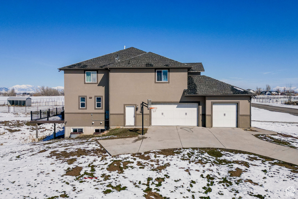 Snow covered house with stucco siding, concrete driveway, and roof with shingles