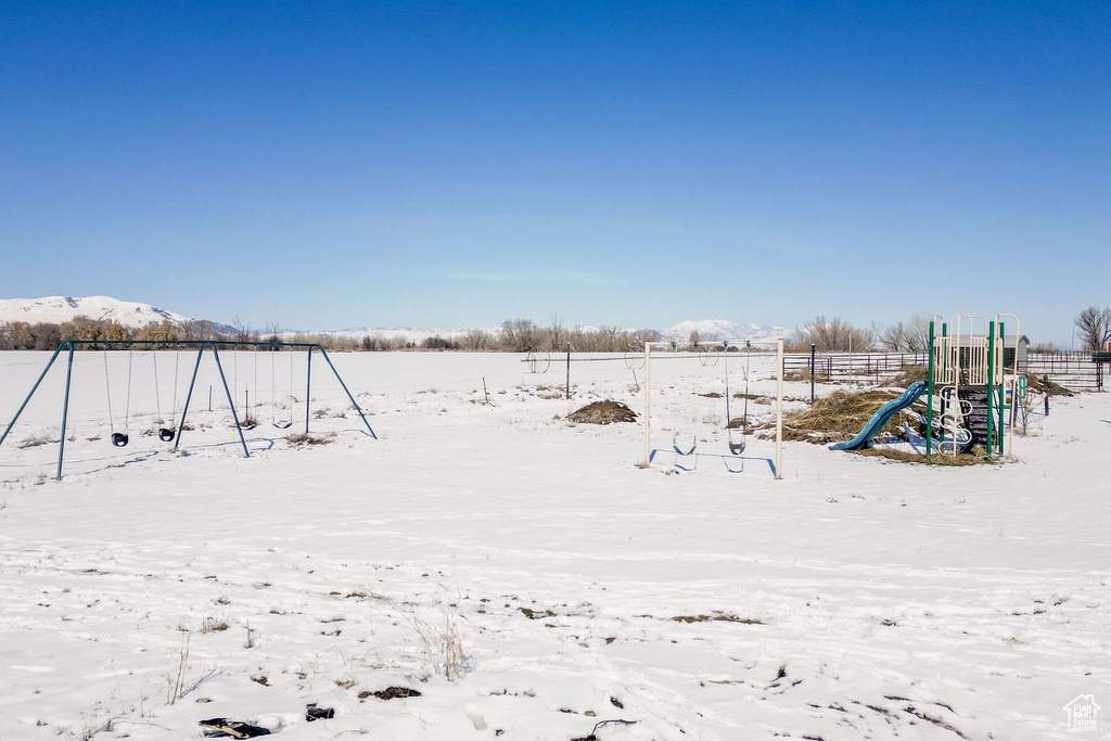 Yard covered in snow featuring playground community and a mountain view