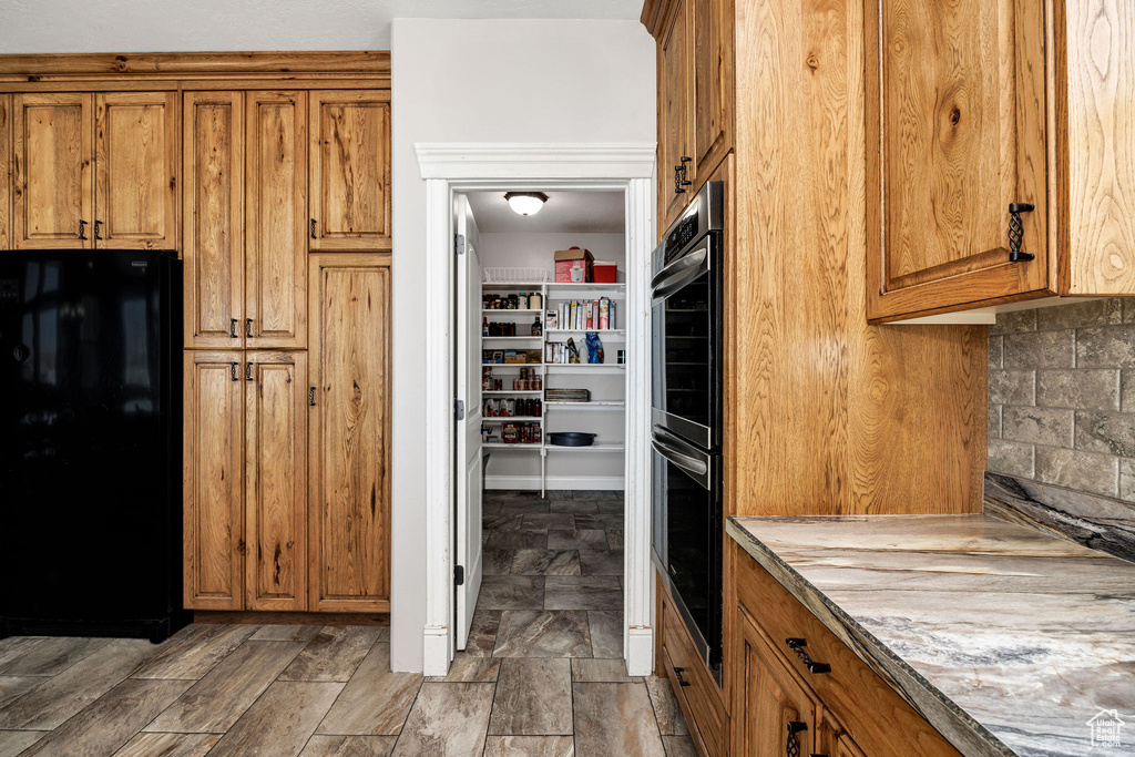 Kitchen with tasteful backsplash, double oven, brown cabinetry, and freestanding refrigerator