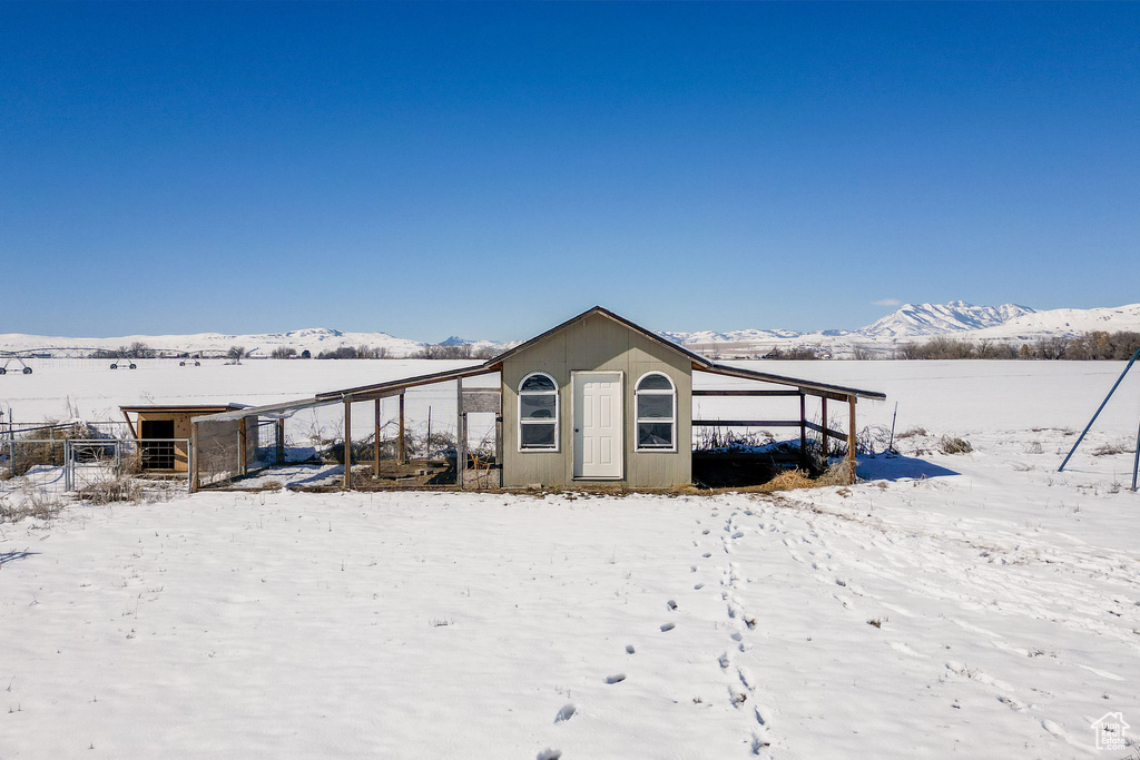 Snow covered property featuring a mountain view, a carport, and an outdoor structure