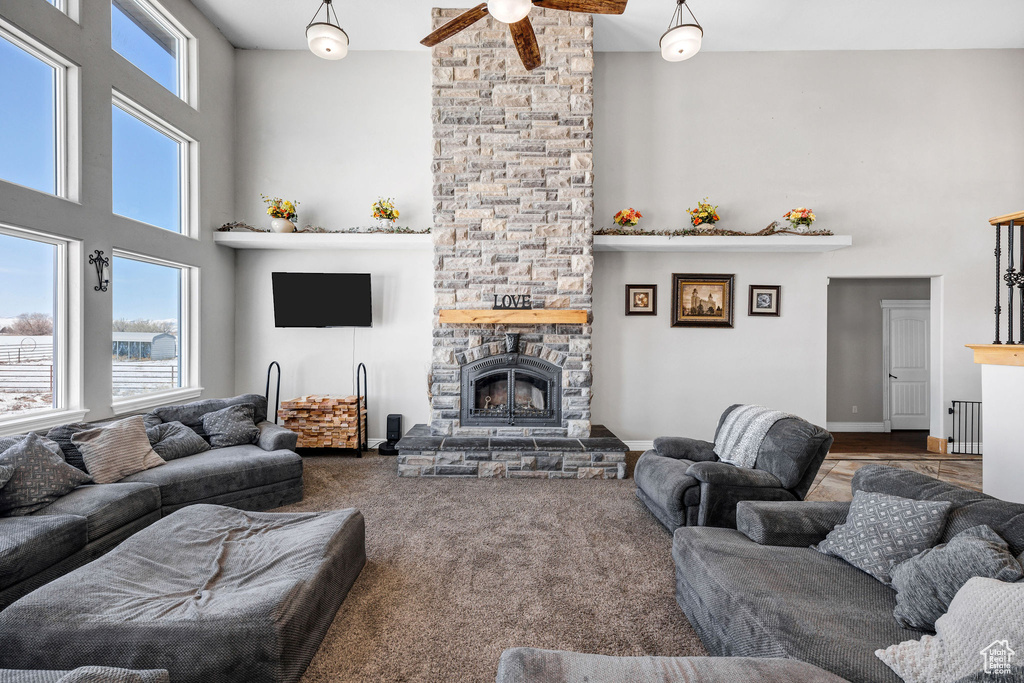 Carpeted living area featuring a stone fireplace, a high ceiling, and ceiling fan