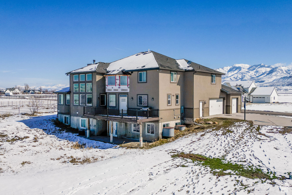 Snow covered back of property with a garage, a mountain view, and stucco siding