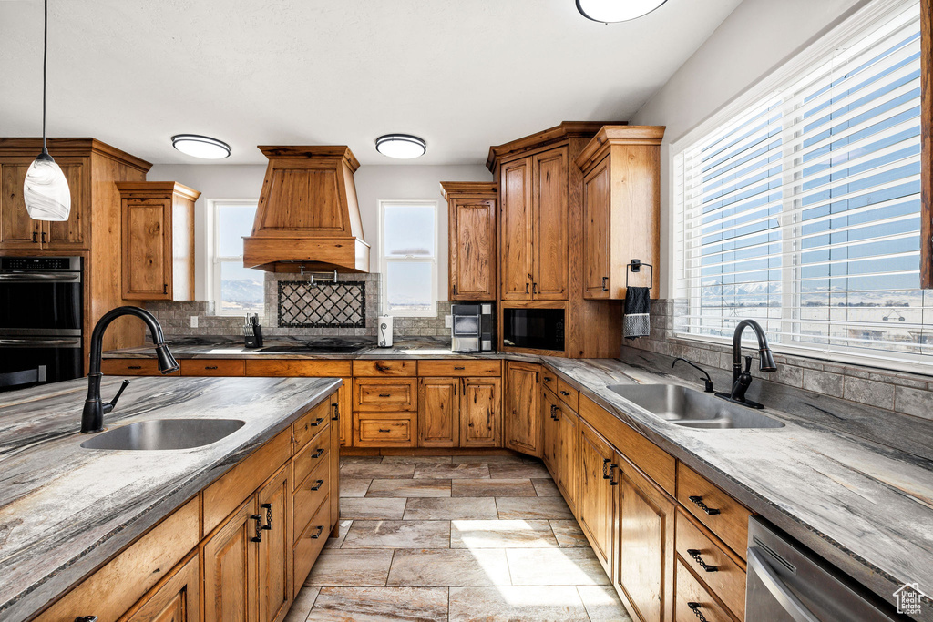 Kitchen with decorative backsplash, black appliances, premium range hood, and a sink