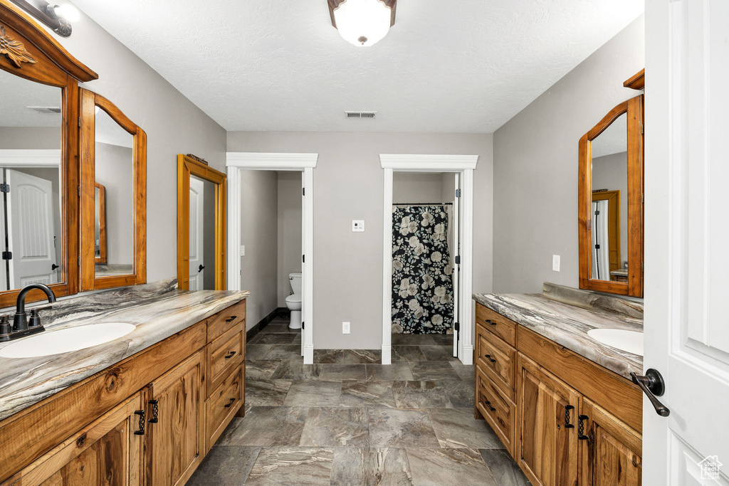 Full bathroom with toilet, two vanities, visible vents, and a sink