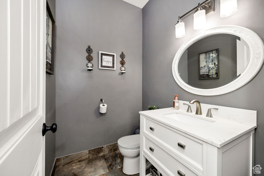 Bathroom with stone finish flooring, toilet, vanity, and baseboards