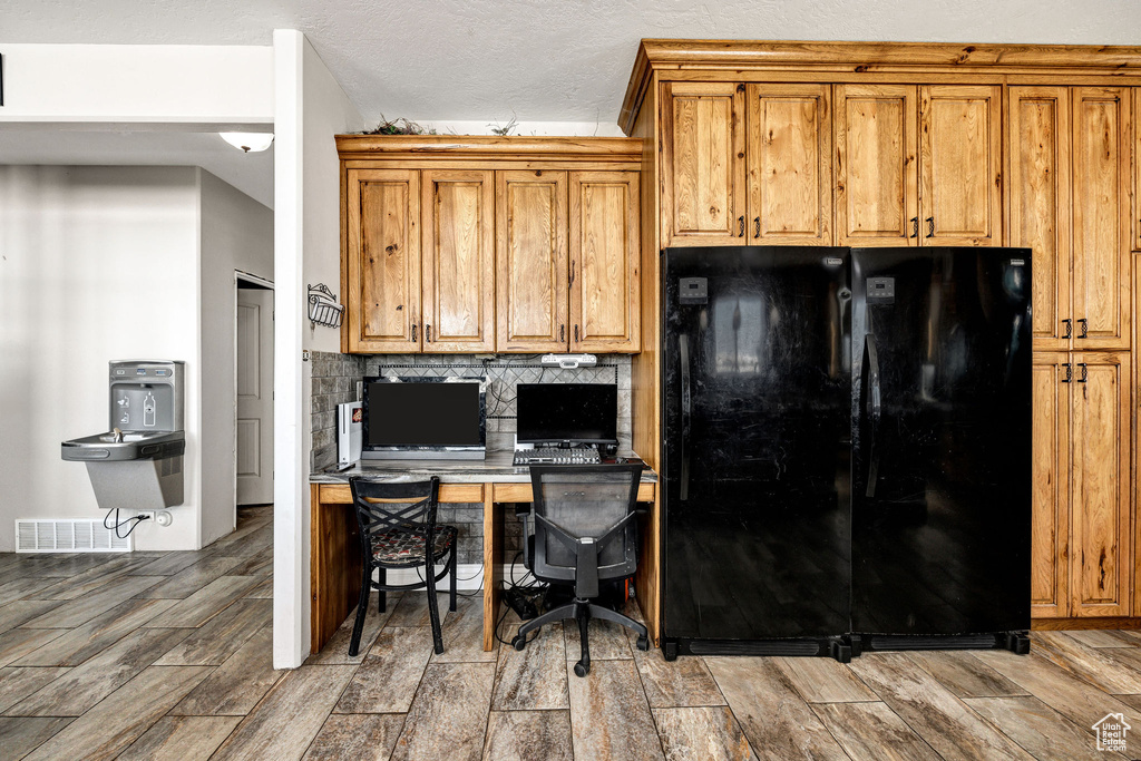 Kitchen with brown cabinetry, visible vents, wood tiled floor, freestanding refrigerator, and decorative backsplash