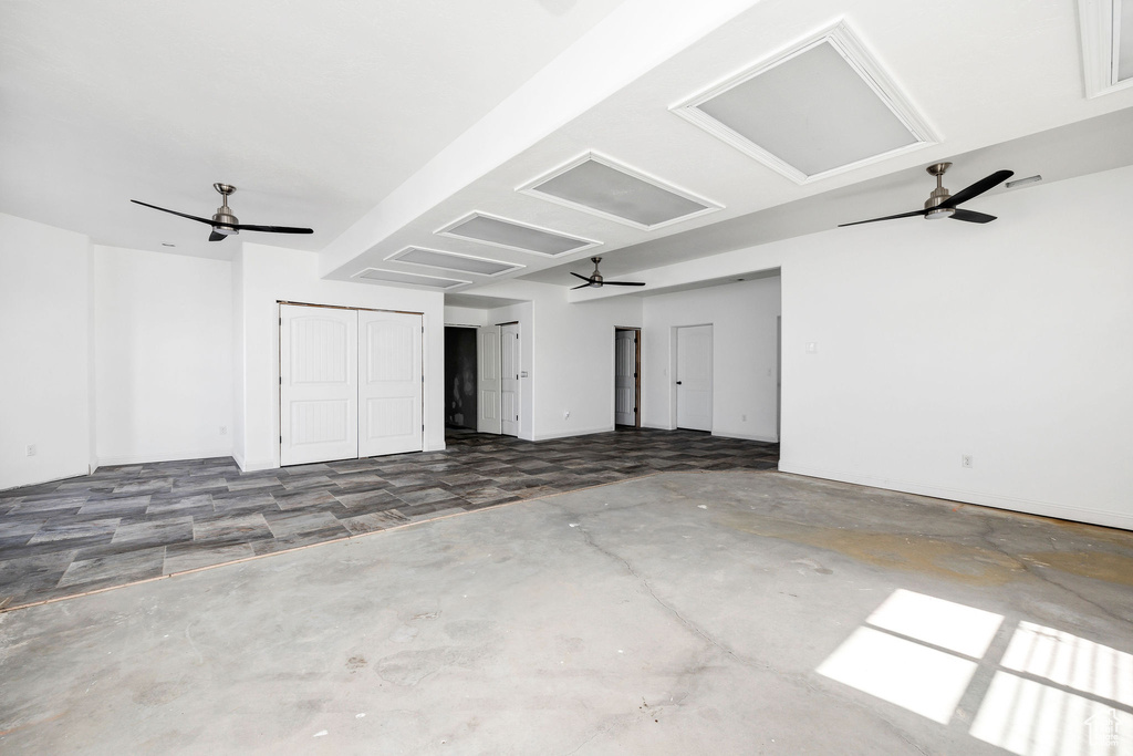 Unfurnished room featuring a ceiling fan, attic access, and unfinished concrete floors