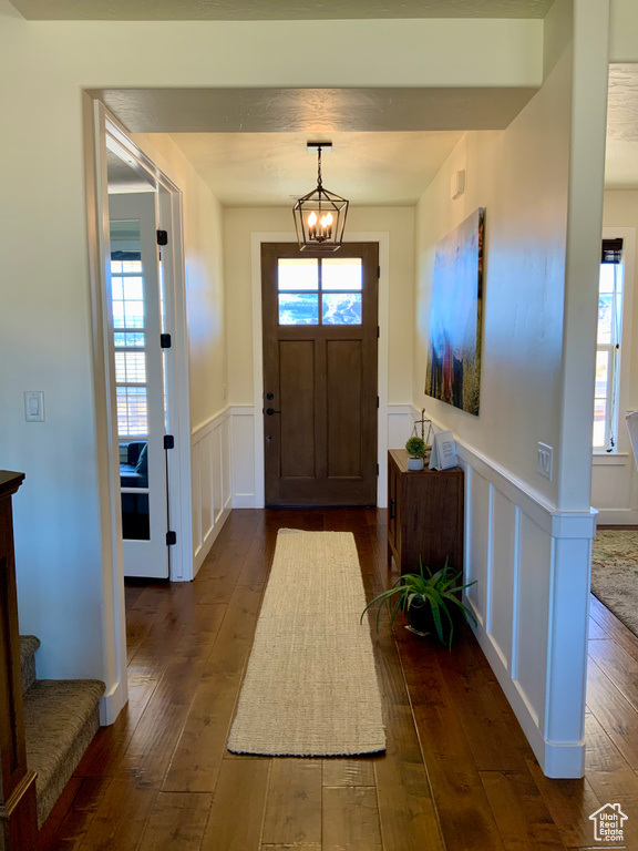 Entryway with dark wood finished floors, stairway, wainscoting, a decorative wall, and a chandelier