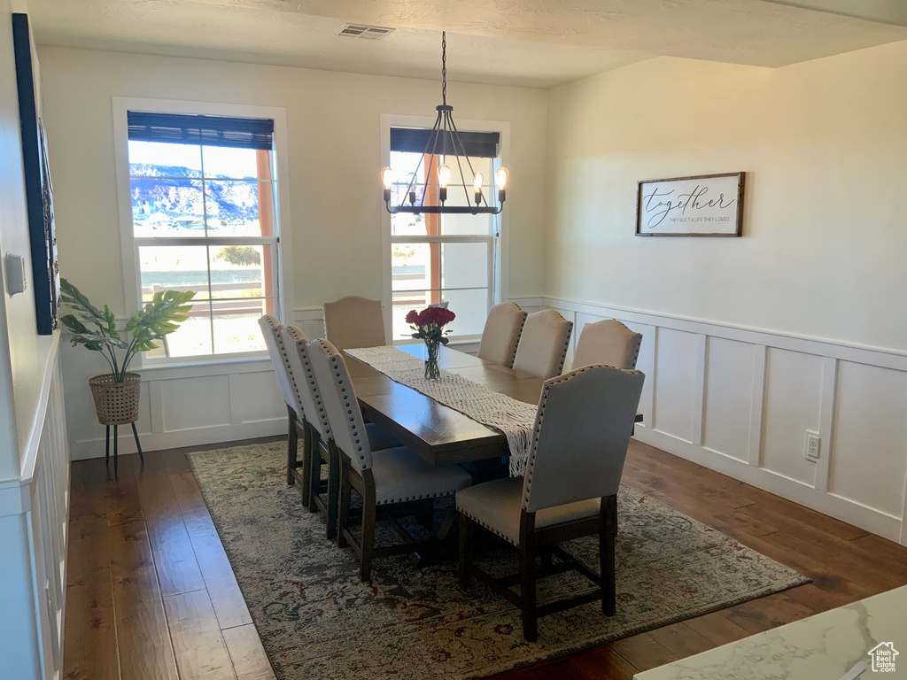 Dining room with visible vents, a decorative wall, a wainscoted wall, a notable chandelier, and dark wood-style flooring