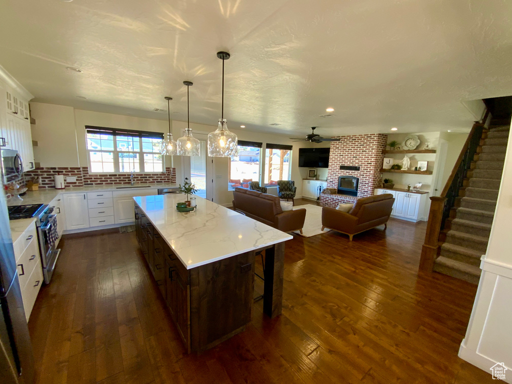 Kitchen featuring white cabinets, a brick fireplace, stainless steel appliances, and dark wood-type flooring