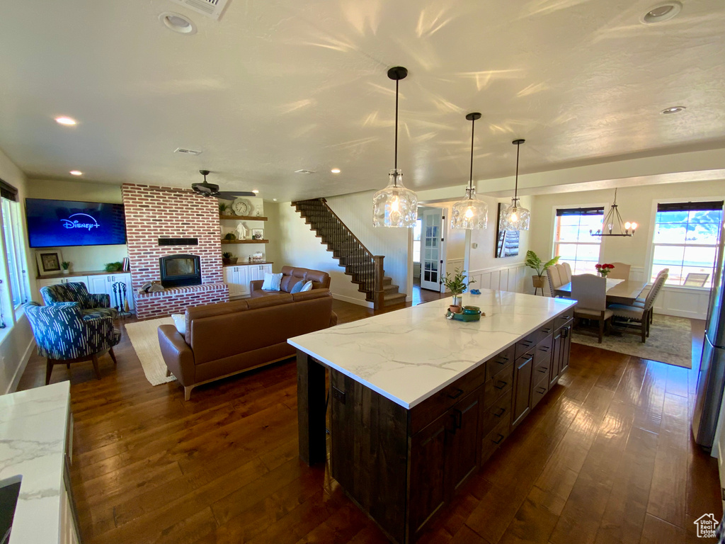 Kitchen with light stone counters, dark brown cabinets, a brick fireplace, and dark wood-type flooring