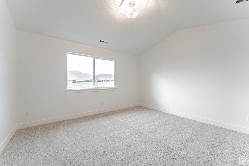 Empty room with vaulted ceiling and light colored carpet