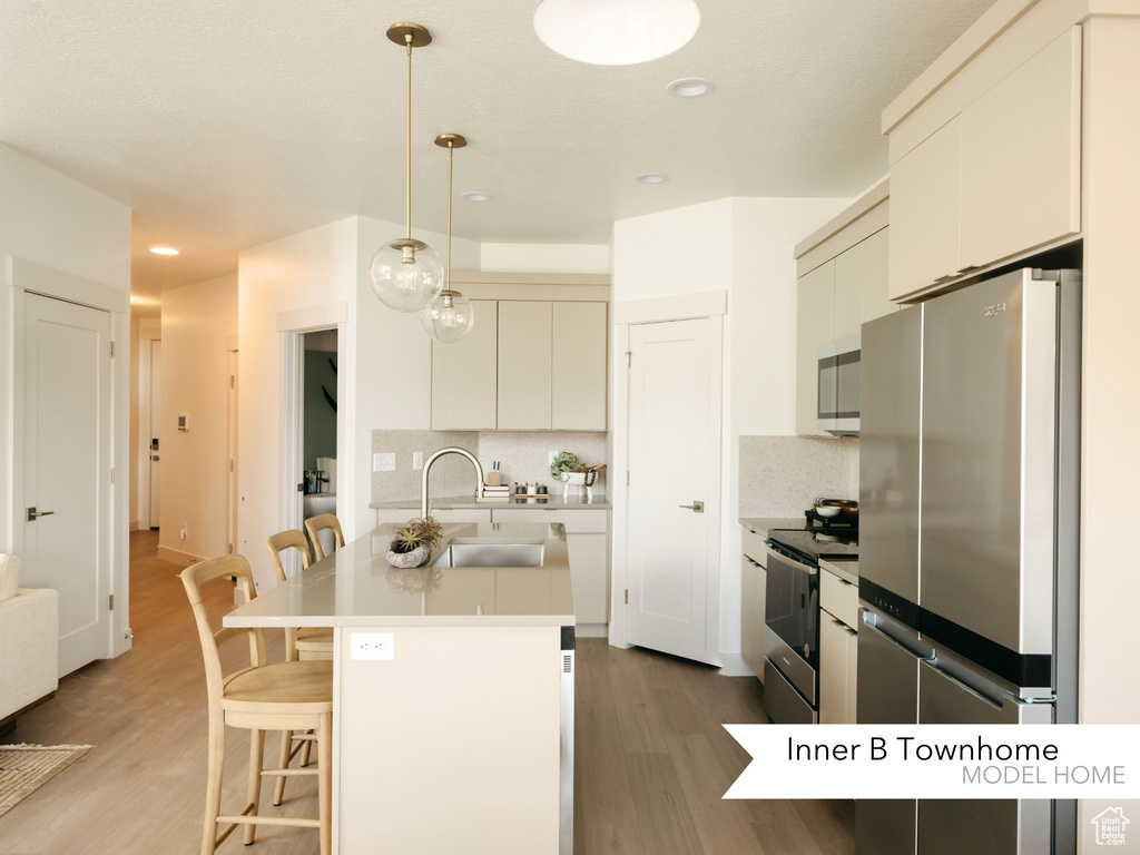 Kitchen with a sink, a kitchen bar, appliances with stainless steel finishes, and light wood finished floors