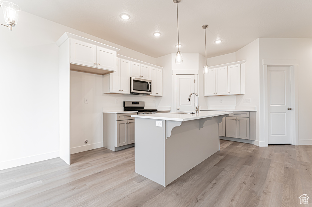 Kitchen featuring stainless steel appliances, light wood-style floors, recessed lighting, light countertops, and a breakfast bar