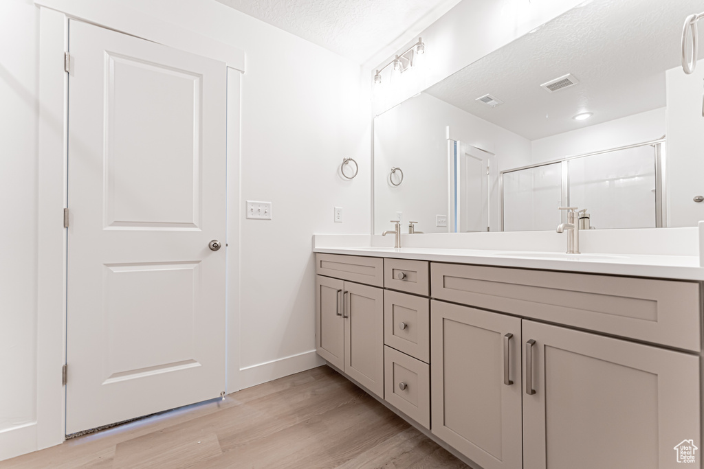 Full bathroom featuring double vanity, wood finished floors, a shower stall, and a textured ceiling