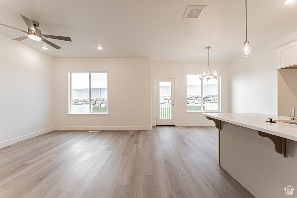 Unfurnished living room with healthy amount of natural light, light wood-type flooring, a chandelier, recessed lighting, and a ceiling fan