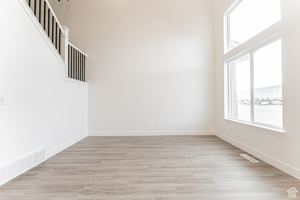Unfurnished room featuring healthy amount of natural light, light wood finished floors, and a towering ceiling