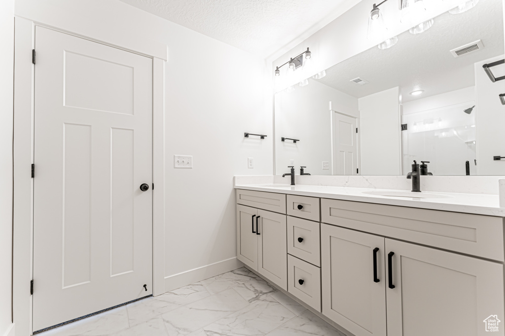 Bathroom with double vanity, marble look tile flooring, a stall shower, and a textured ceiling