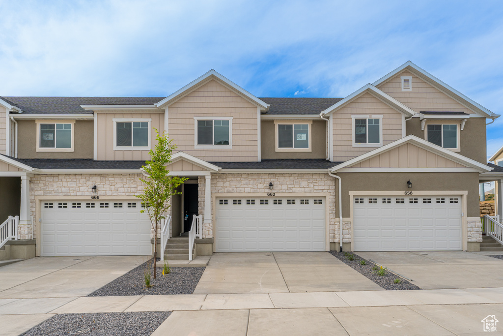 View of property featuring board and batten siding, stone siding, a garage, and concrete driveway