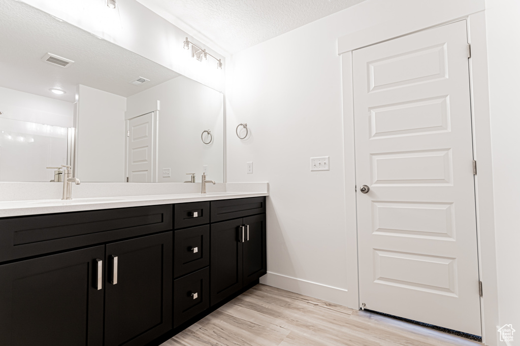 Full bath with double vanity, wood finished floors, and a textured ceiling