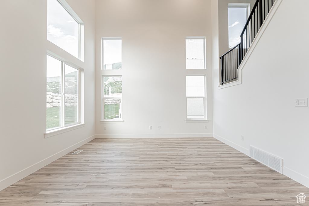 Empty room featuring a towering ceiling, light wood-type flooring, and stairway