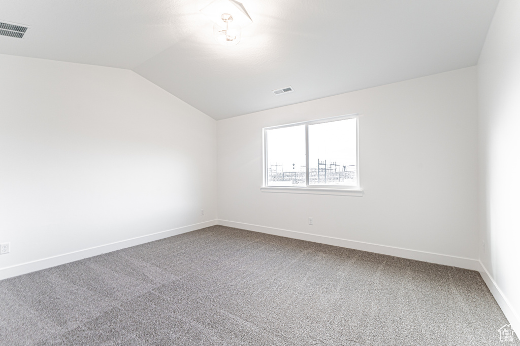 Carpeted spare room with vaulted ceiling and baseboards