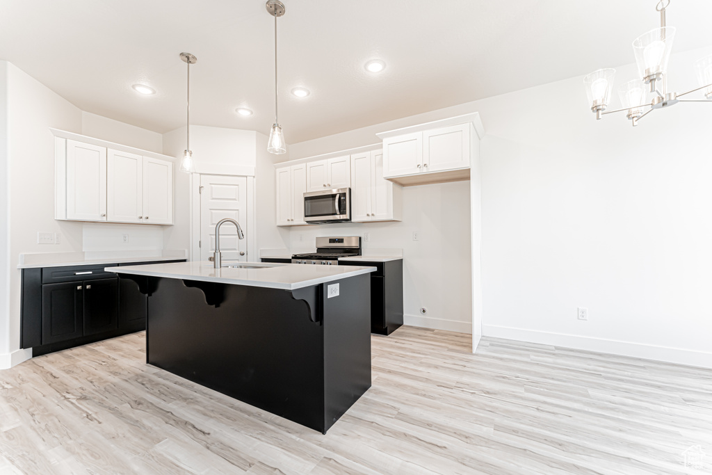 Kitchen featuring appliances with stainless steel finishes, light countertops, light wood-style floors, dark cabinets, and white cabinetry