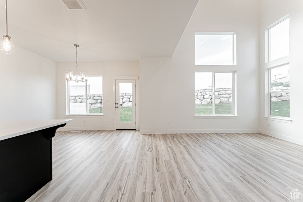 Unfurnished living room featuring light wood finished floors, a chandelier, plenty of natural light, and a high ceiling