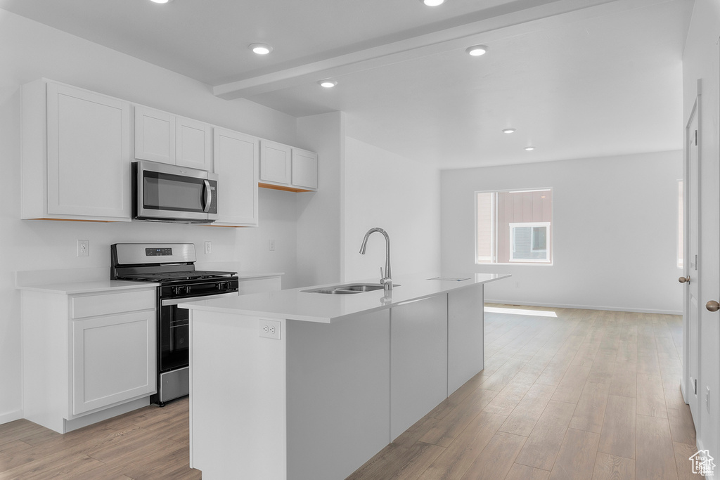 Kitchen featuring an island with sink, a sink, white cabinets, light wood-style floors, and appliances with stainless steel finishes