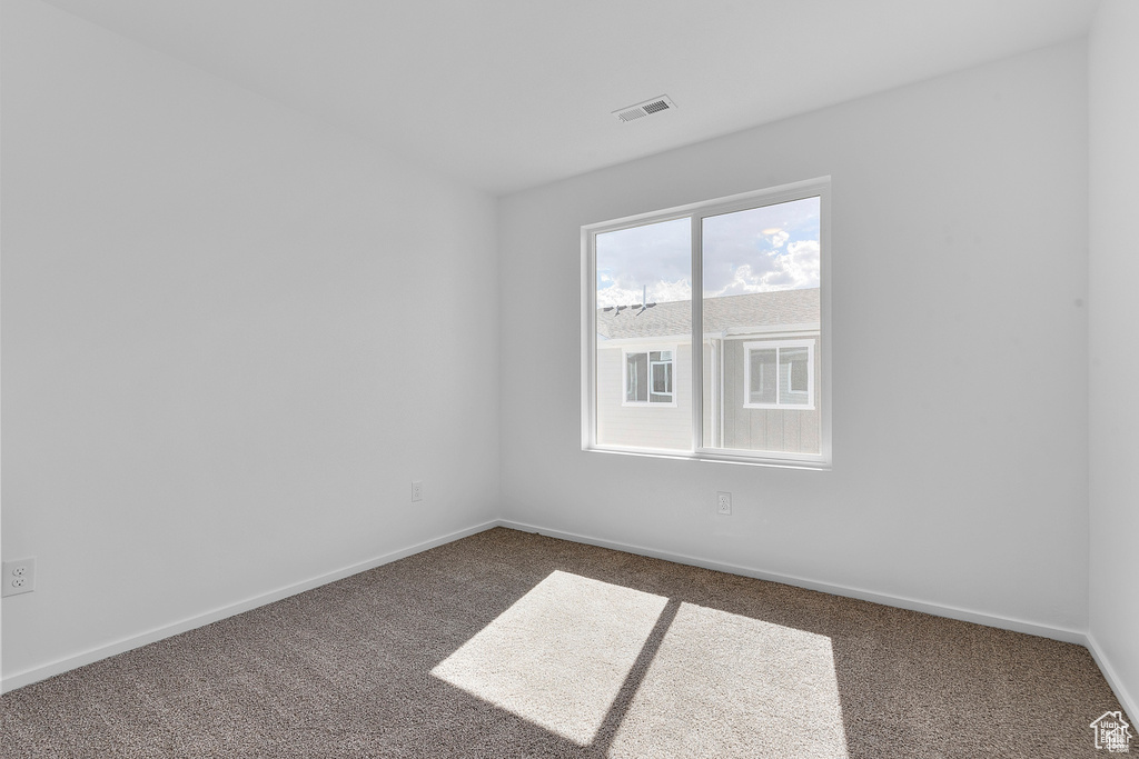 Empty room with baseboards, visible vents, and dark carpet