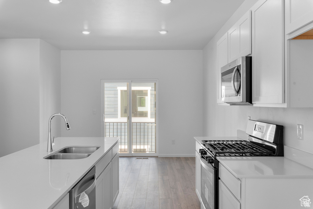 Kitchen with a sink, light countertops, white cabinets, appliances with stainless steel finishes, and light wood-type flooring