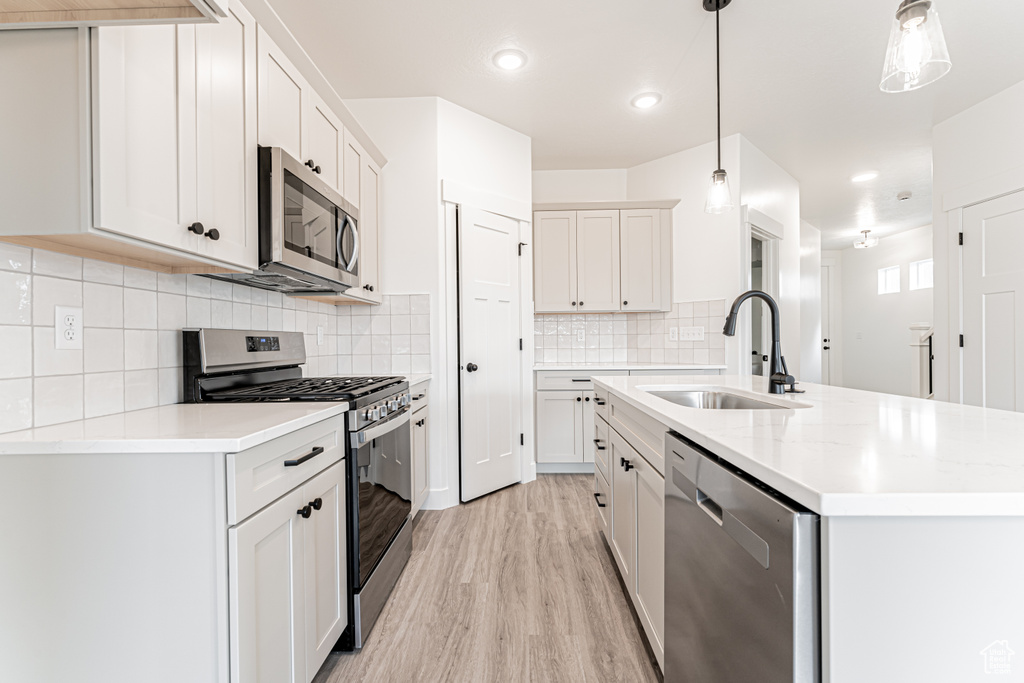 Kitchen featuring appliances with stainless steel finishes, light wood-style flooring, a kitchen island with sink, decorative backsplash, and pendant lighting