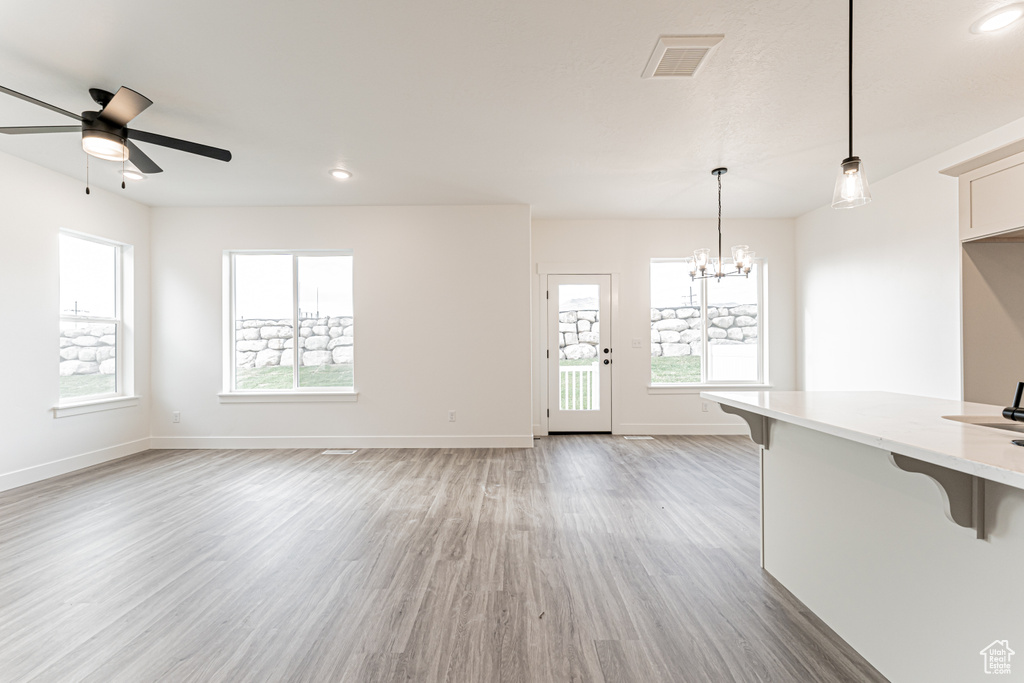 Unfurnished living room featuring light wood-style flooring, plenty of natural light, ceiling fan, a chandelier, and recessed lighting