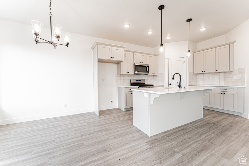 Kitchen with stainless steel appliances, light wood finished floors, a breakfast bar area, a chandelier, and light countertops