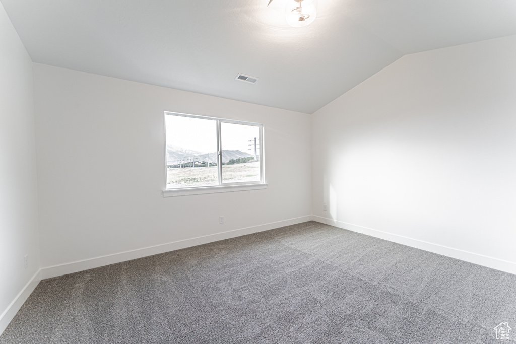 Empty room featuring vaulted ceiling and carpet flooring