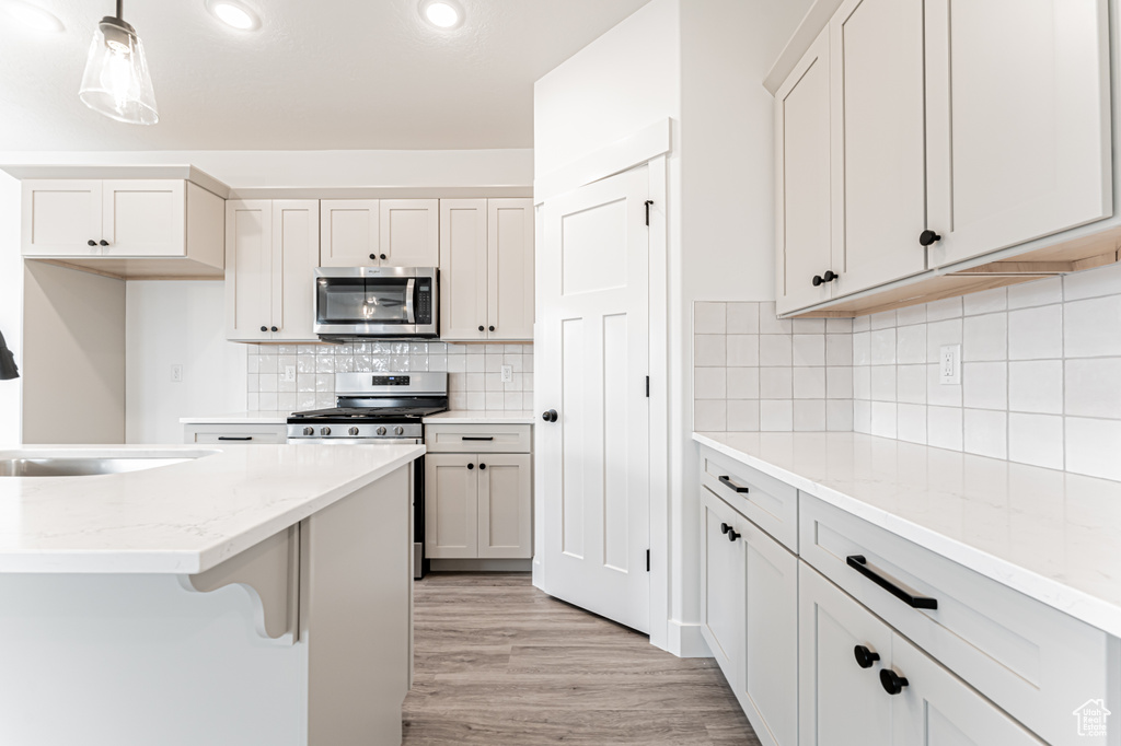 Kitchen with stainless steel appliances, light wood-style floors, light stone countertops, backsplash, and recessed lighting